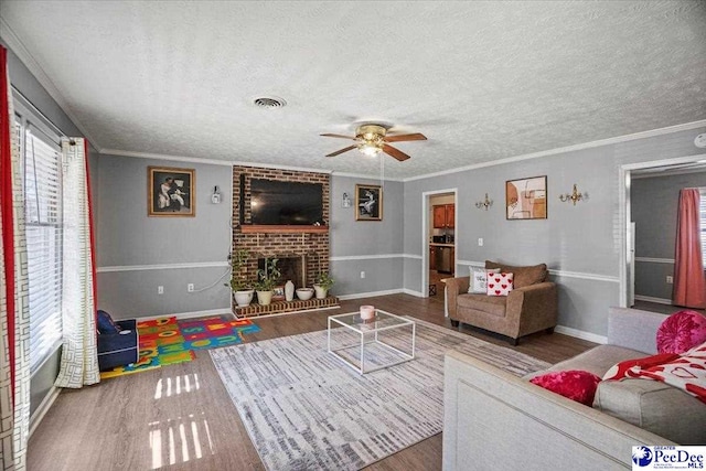 living room featuring a brick fireplace, crown molding, wood-type flooring, and a textured ceiling