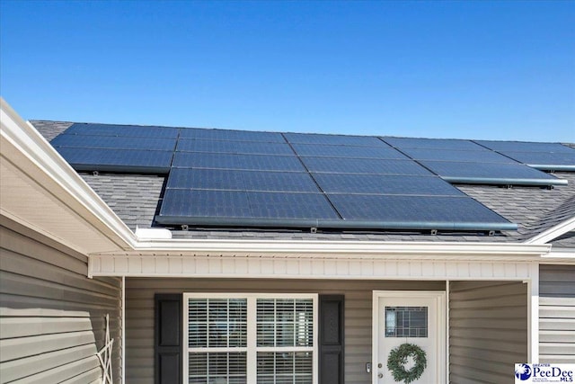 entrance to property featuring solar panels and roof with shingles