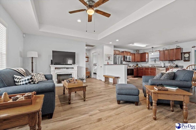 living room with ceiling fan, light wood-style flooring, recessed lighting, a premium fireplace, and a raised ceiling