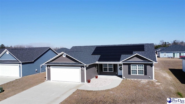 ranch-style home featuring concrete driveway, roof with shingles, an attached garage, and solar panels