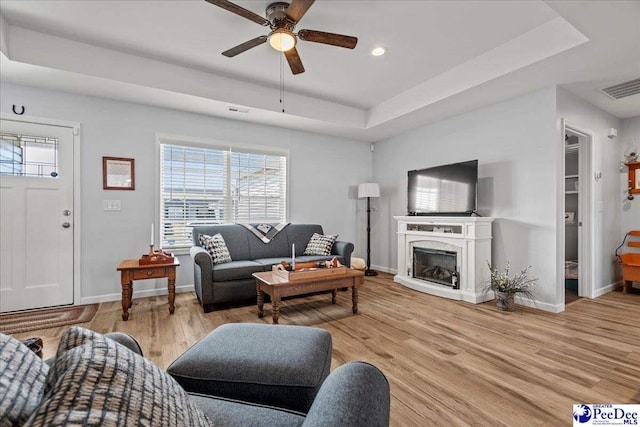 living room featuring light wood-style flooring, a fireplace, a raised ceiling, and visible vents