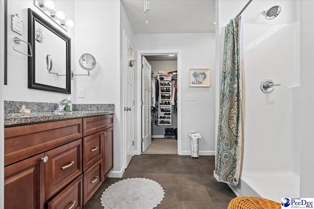 bathroom with a shower with curtain, baseboards, a walk in closet, and vanity