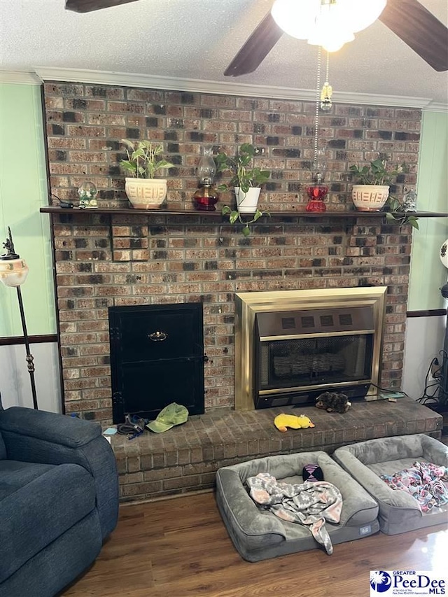 living room with ceiling fan, ornamental molding, wood finished floors, a textured ceiling, and a brick fireplace