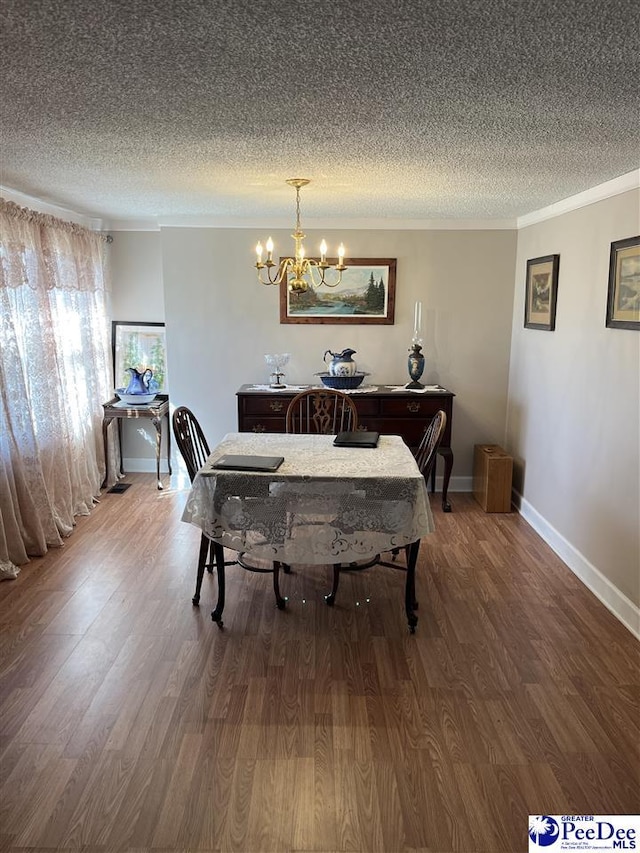 dining area with ornamental molding, a notable chandelier, a textured ceiling, and wood finished floors