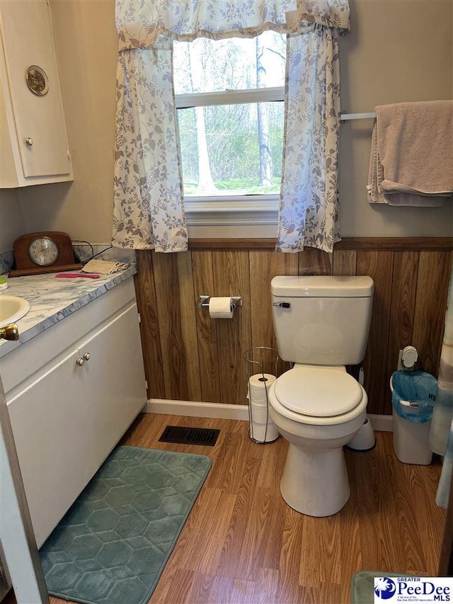 half bath featuring toilet, a wainscoted wall, wood walls, wood finished floors, and visible vents