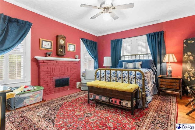 bedroom with a fireplace, wood-type flooring, ornamental molding, and ceiling fan