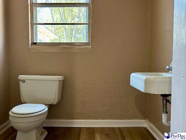 half bath with toilet, a sink, baseboards, and wood finished floors