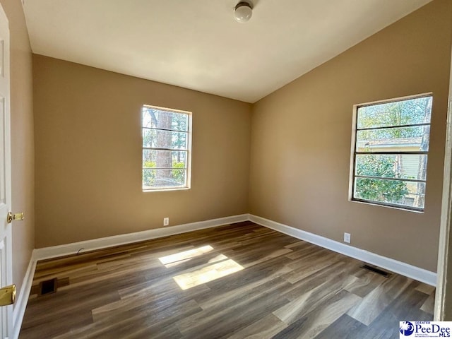 spare room with dark wood-type flooring, visible vents, and vaulted ceiling