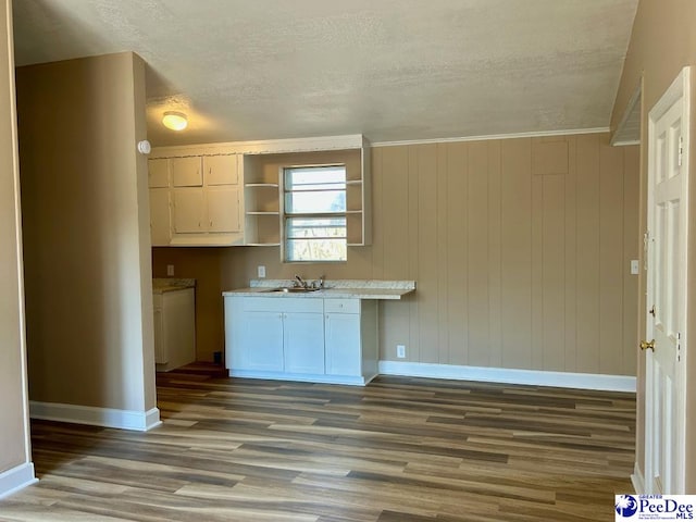 kitchen featuring open shelves, light countertops, a sink, wood finished floors, and baseboards