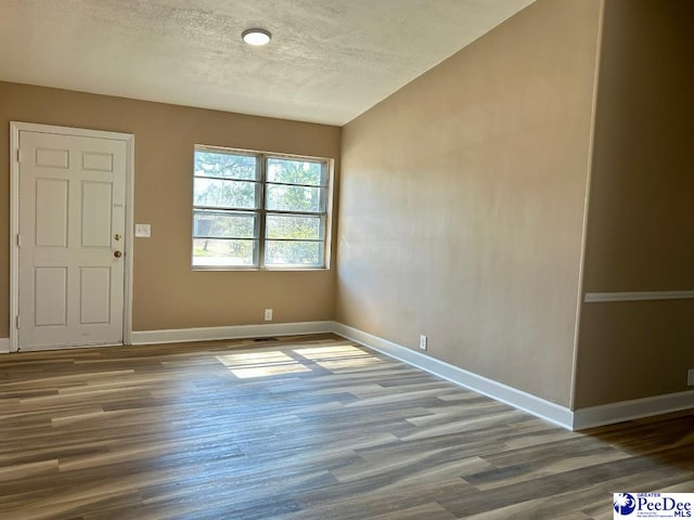 empty room featuring a textured ceiling, baseboards, and wood finished floors