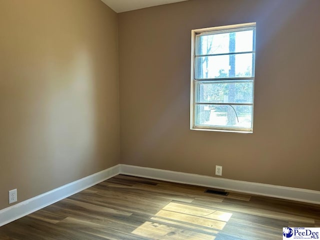 empty room with dark wood-style flooring, visible vents, and baseboards