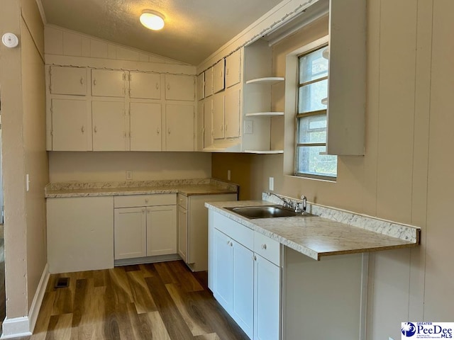 kitchen with white cabinets, dark wood-style flooring, vaulted ceiling, light countertops, and a sink