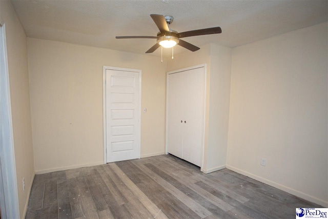 unfurnished bedroom featuring baseboards, ceiling fan, wood finished floors, a textured ceiling, and a closet