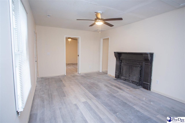 unfurnished living room featuring ceiling fan, baseboards, a fireplace with flush hearth, and light wood-style floors