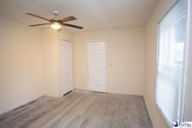 spare room featuring light wood finished floors, a ceiling fan, and baseboards