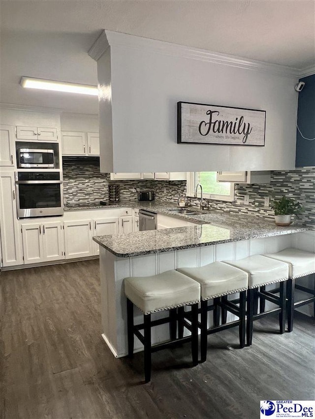 kitchen with appliances with stainless steel finishes, a peninsula, dark wood-style floors, crown molding, and light stone countertops
