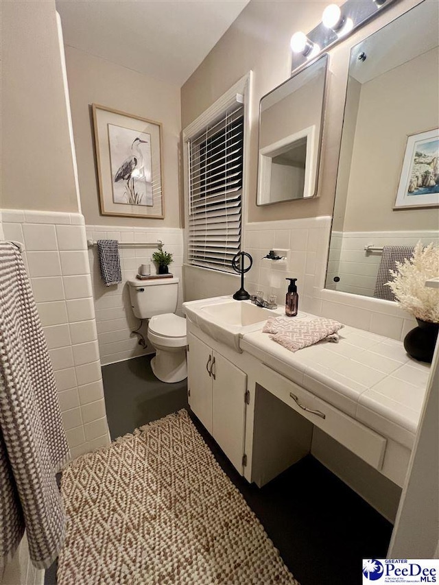 bathroom featuring toilet, vanity, a wainscoted wall, and tile walls