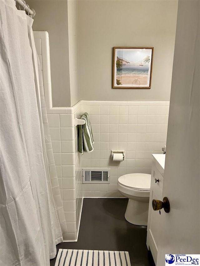full bathroom featuring vanity, visible vents, toilet, wainscoting, and tile walls