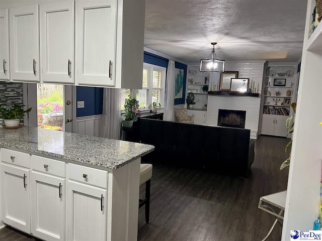 kitchen with dark wood-style flooring, a peninsula, white cabinetry, and light stone counters