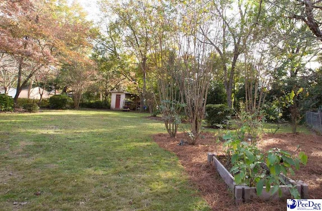 view of yard featuring a garden, an outdoor structure, fence, and a storage unit