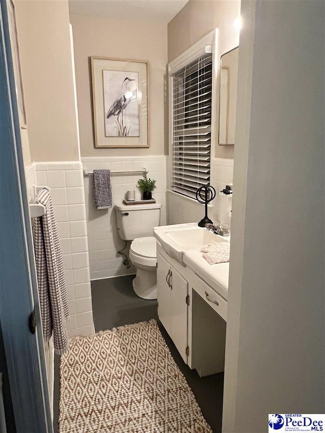 bathroom featuring tile walls, toilet, vanity, and a wainscoted wall