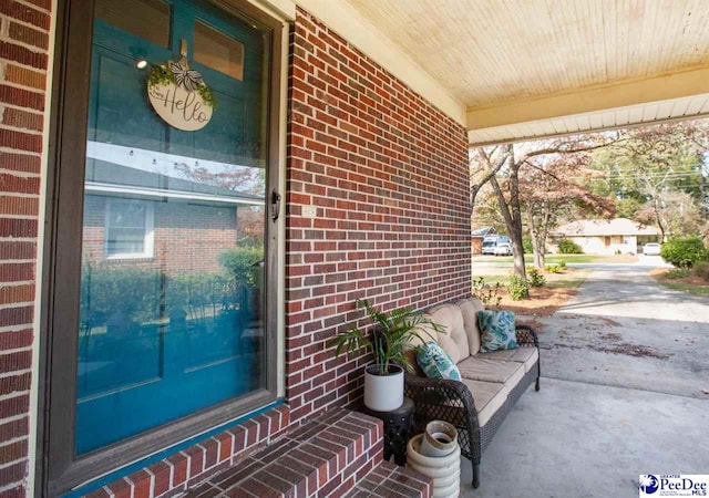 view of exterior entry with brick siding, covered porch, and an outdoor hangout area