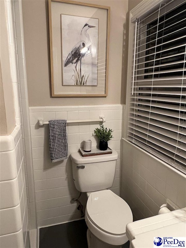 bathroom with toilet, a wainscoted wall, and tile walls