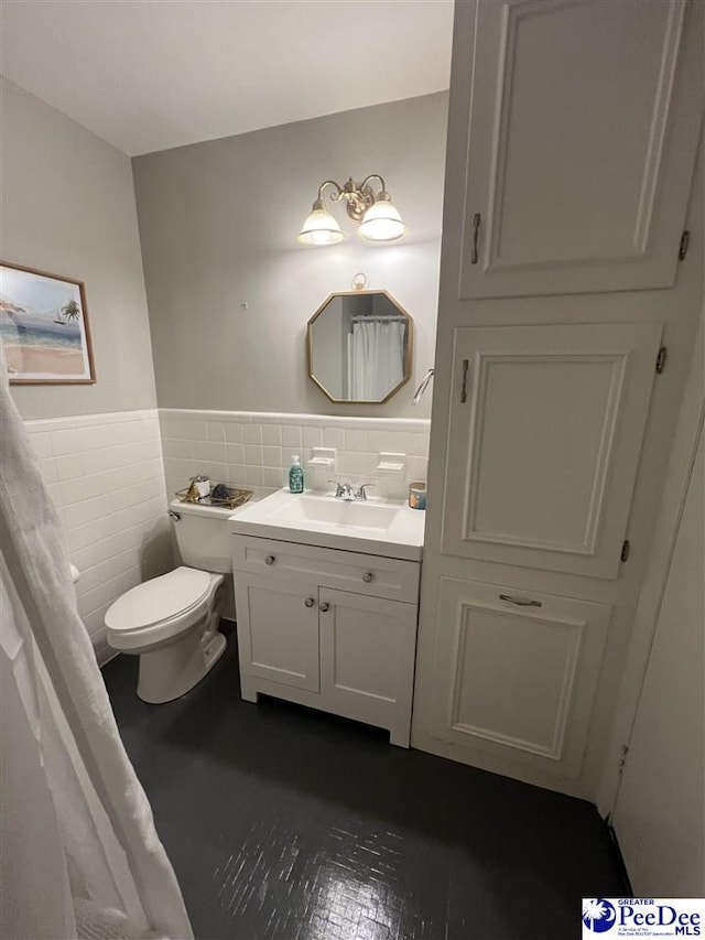 bathroom with toilet, vanity, wainscoting, and tile walls