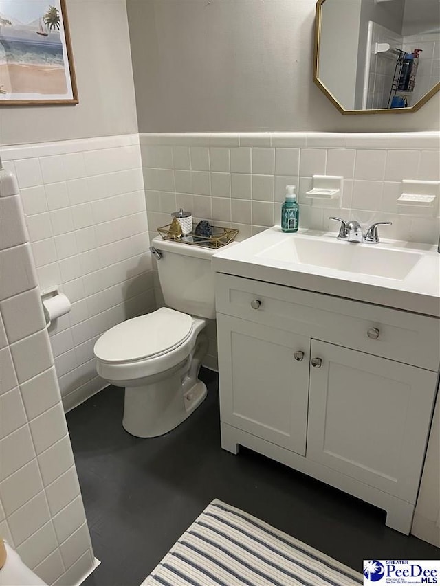 bathroom featuring toilet, vanity, wainscoting, and tile walls