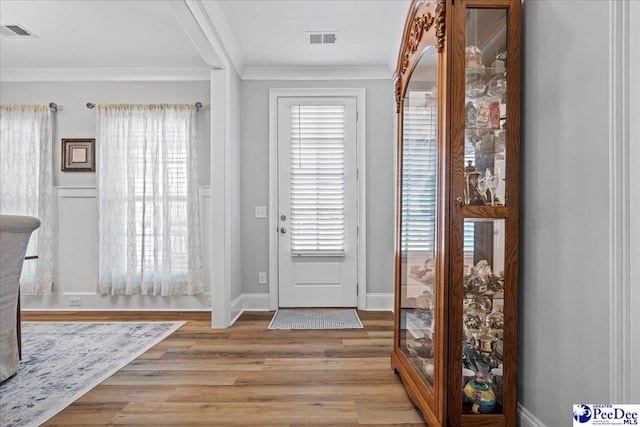 foyer entrance with visible vents, baseboards, wood finished floors, and crown molding