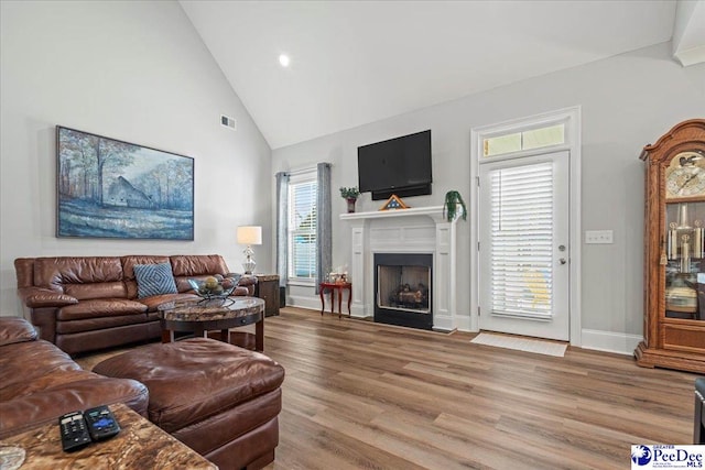 living area featuring visible vents, baseboards, a fireplace with flush hearth, wood finished floors, and high vaulted ceiling