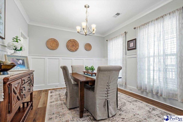 dining space with a notable chandelier, wood finished floors, visible vents, and ornamental molding