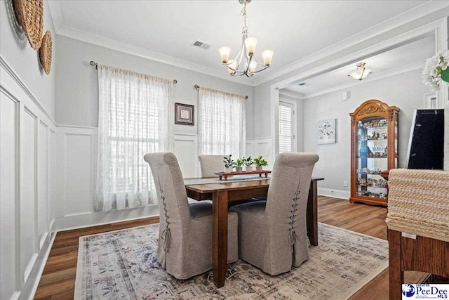 dining space with wood finished floors, visible vents, crown molding, a decorative wall, and a notable chandelier