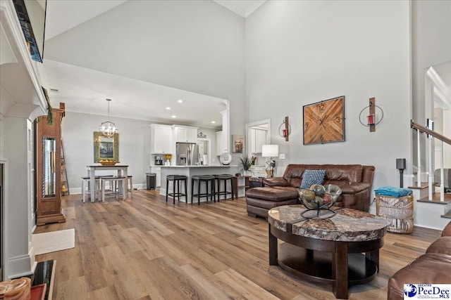 living area featuring stairway, baseboards, an inviting chandelier, a high ceiling, and light wood-type flooring