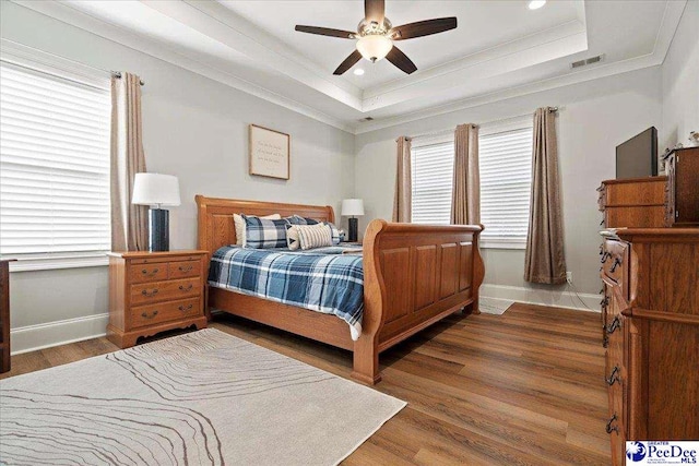 bedroom featuring a tray ceiling, crown molding, wood finished floors, and baseboards