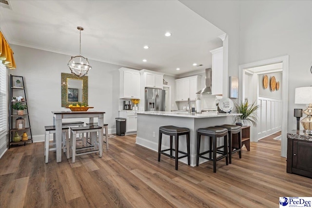 kitchen with ornamental molding, stainless steel refrigerator with ice dispenser, wood finished floors, a peninsula, and wall chimney exhaust hood