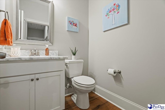 half bathroom featuring toilet, vanity, baseboards, and wood finished floors