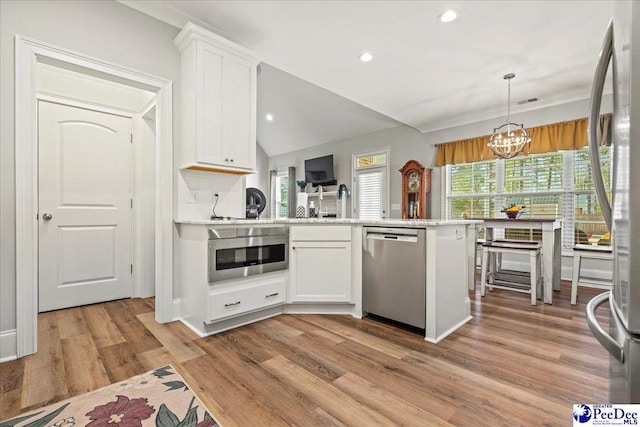 kitchen with light wood finished floors, a peninsula, stainless steel appliances, light countertops, and white cabinetry