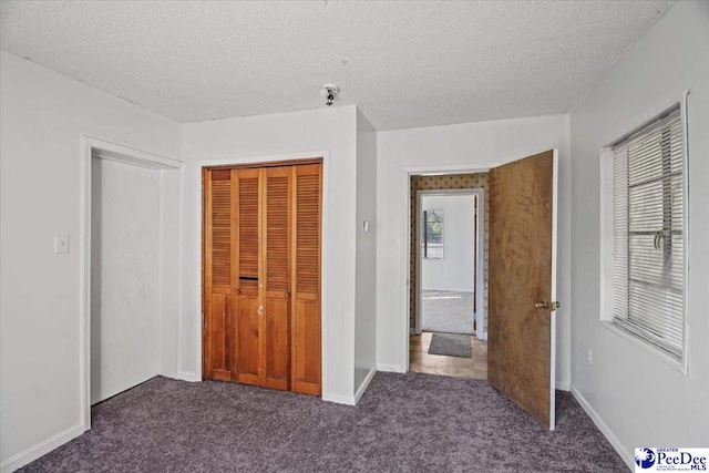 unfurnished bedroom with dark colored carpet, a textured ceiling, and a closet