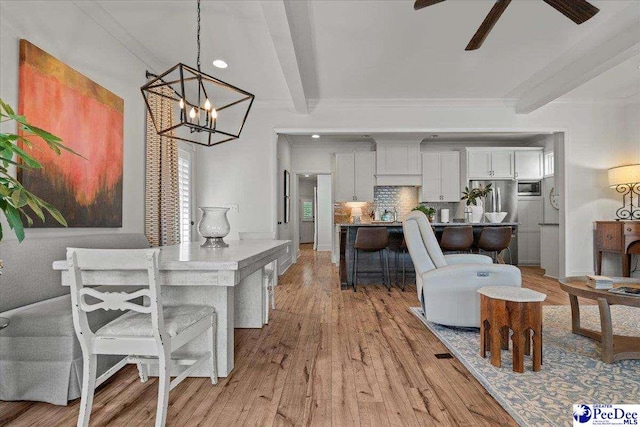 dining area featuring ceiling fan with notable chandelier, beam ceiling, light wood finished floors, and crown molding