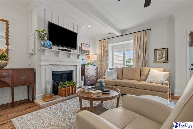 living room with a tile fireplace, ornamental molding, wood finished floors, and beam ceiling
