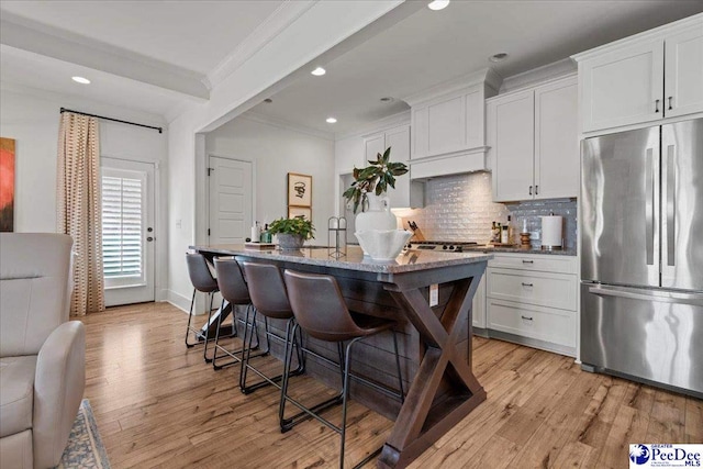 kitchen with crown molding, decorative backsplash, light wood-type flooring, a breakfast bar area, and stainless steel refrigerator