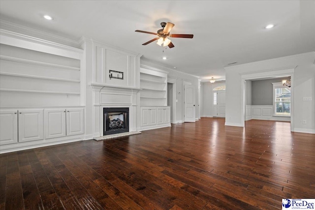 unfurnished living room featuring hardwood / wood-style flooring, a large fireplace, built in features, ceiling fan with notable chandelier, and ornamental molding