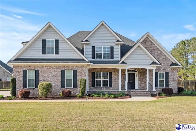craftsman inspired home with a front yard, covered porch, fence, and brick siding