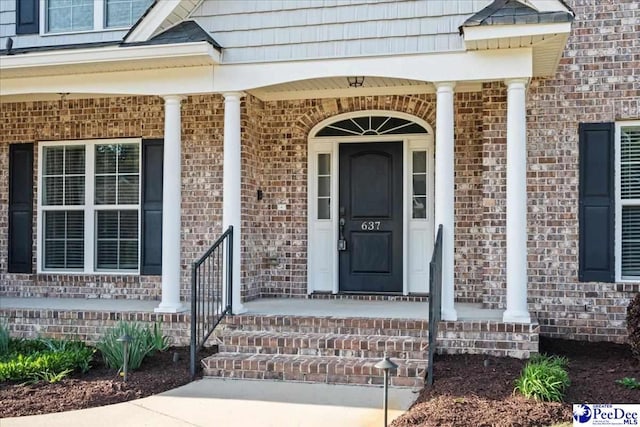 view of exterior entry with brick siding and a porch