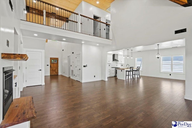 unfurnished living room with dark wood-type flooring, sink, a notable chandelier, and a towering ceiling