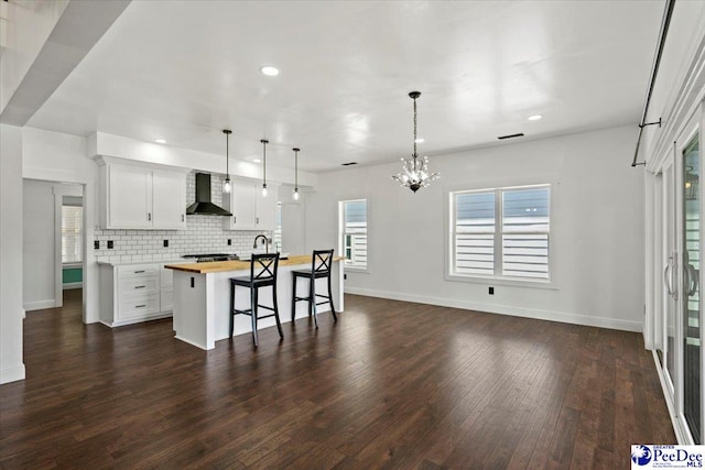 kitchen featuring a kitchen island, pendant lighting, wood counters, white cabinetry, and wall chimney range hood