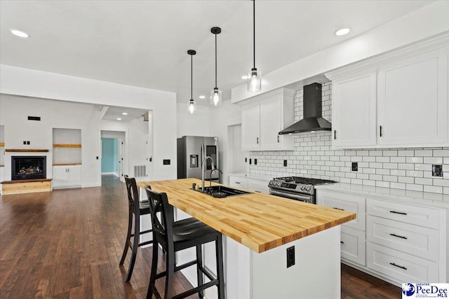 kitchen with stainless steel appliances, an island with sink, white cabinets, and wall chimney exhaust hood