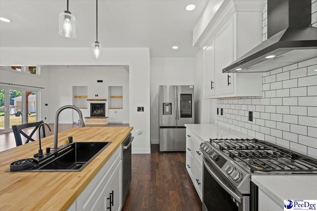 kitchen featuring butcher block counters, sink, appliances with stainless steel finishes, wall chimney range hood, and white cabinets