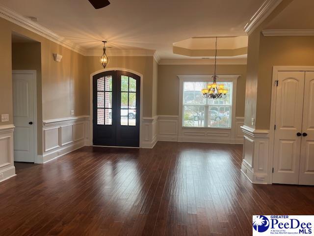 entrance foyer with dark hardwood / wood-style flooring, ornamental molding, a chandelier, and french doors